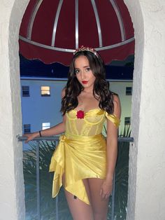 a woman in a yellow costume standing on a balcony with an umbrella over her head