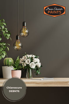 three light bulbs hanging over a table with flowers in vases and potted plants