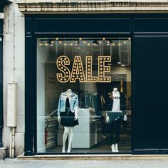 a store front with mannequins in the window and a sale sign on display