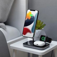 an iphone and wireless charging station on a white table next to a plant in a vase