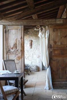 an old room with wooden doors and white drapes hanging from the ceiling in front of a table