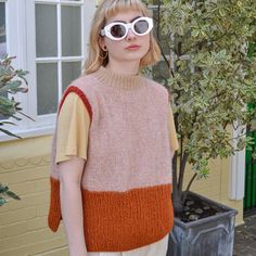 a woman wearing sunglasses standing in front of a tree and potted plant with her hand on her hip