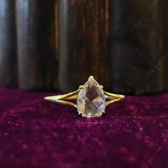 a yellow gold ring with an oval cut stone in the center on a purple velvet surface