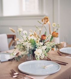 the table is set with plates, silverware and flowers