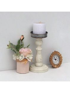 there is a candle and some flowers on the shelf next to each other with a clock