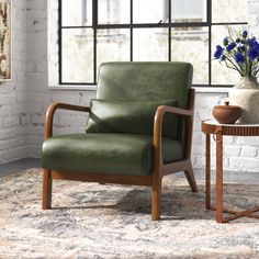 a green chair sitting in front of a window next to a table with flowers on it