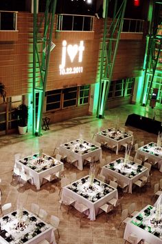 tables and chairs are set up in the center of an indoor event space with green lighting