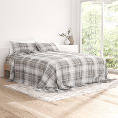 a bed with plaid sheets and pillows in a white room next to a large window