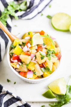 a white bowl filled with pineapple salsa next to sliced limes and cilantro