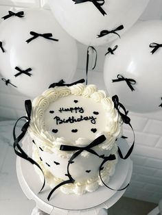 a birthday cake with white frosting and black ribbon on top, surrounded by balloons