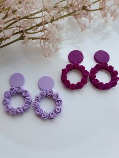 two pairs of earrings sitting on top of a white table next to pink and purple flowers