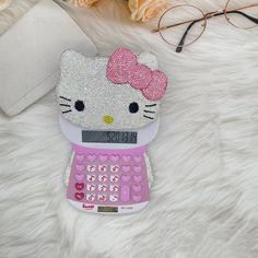 a hello kitty cell phone case sitting on top of a white fur covered floor next to glasses