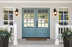 two large planters with flowers are in front of a blue door and white pillars