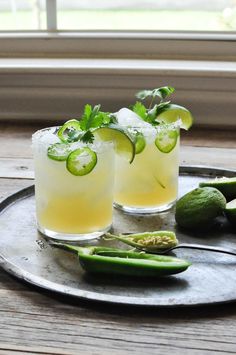 two glasses filled with lemonade and cucumber on a metal tray next to green peppers