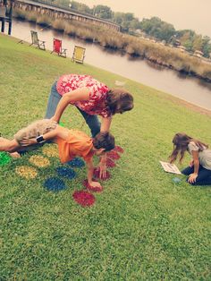 three people in the grass playing with colored paper on the ground next to a body of water