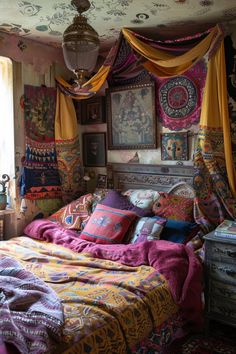 a bed covered in lots of colorful blankets next to a window with curtains over it