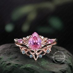 a pink ring sitting on top of a rock with green leaves and stones around it