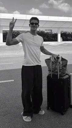 a man standing next to a black suitcase and giving the peace sign with his hand