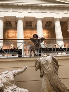 a woman standing on top of a balcony next to two statues in front of a building