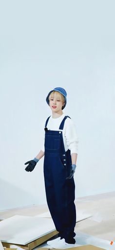 a young boy in overalls and a hat is standing on a piece of cardboard