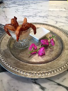 a silver tray topped with food and flowers on top of a marble countertop next to a glass bowl