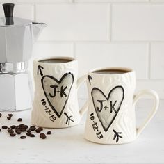 two coffee mugs with designs on them next to some coffee beans and a grinder