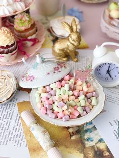 a table topped with lots of cupcakes and other desserts next to a clock