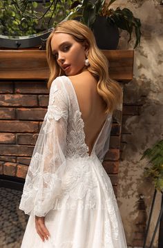 a woman in a white wedding dress standing next to a brick fire place with her back turned towards the camera