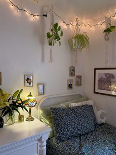 a living room filled with lots of plants on the wall and lights hanging from the ceiling