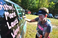 a woman writing on the side of a car with pink marker and green stickers