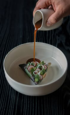 someone is pouring sauce on some food in a white bowl with green and red toppings