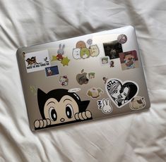 an open laptop computer sitting on top of a white bed covered in lots of stickers