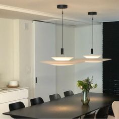 a dining room table with four lights hanging from it's ceiling and flowers in a vase on the table