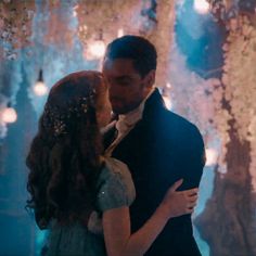 a man and woman standing next to each other in front of a tree filled with lights