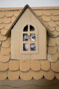 a cardboard house with two cats in the window