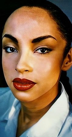 a woman with dark hair and red lipstick wearing a white shirt is looking at the camera