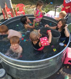 several children are playing in a large metal tub filled with water and toys while others look on