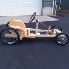 a wooden pedal car is parked in front of a garage with its wheels still attached