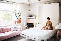 a woman sitting on top of a bed next to a pink couch in a bedroom