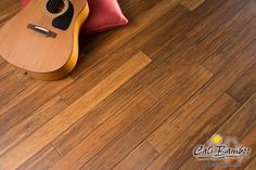 a guitar sitting on top of a wooden floor next to a red pillow and pillows