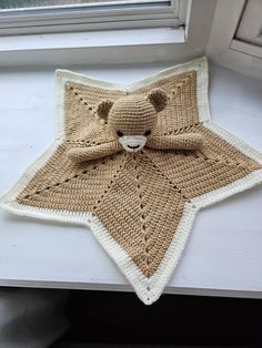 a crocheted teddy bear sitting on top of a star shaped rug in front of a window