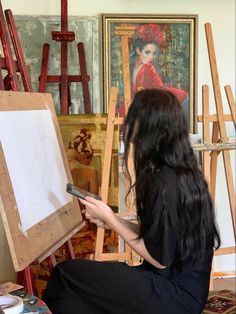 a woman sitting in front of an easel holding a cell phone