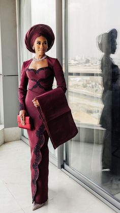 a woman standing in front of a window wearing a purple dress and hat with matching purse