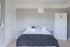 a white bed sitting in a bedroom next to a wall mounted cabinet under a light