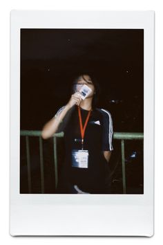 a polaroid photo of a person drinking from a cup with an orange lanyard around his neck