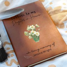 a brown book with flowers on it next to a pen and inkwell, which reads letters to my daughter in heaven