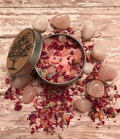 a tin filled with lots of pink flowers on top of a wooden table next to rocks