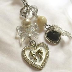 three charms with bows and pearls on a white cloth background, one has a heart shaped brooch