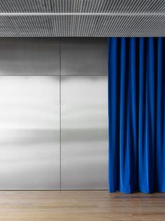 a blue curtain hanging from the side of a metal wall next to a wooden floor