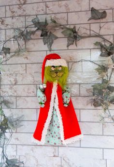 a green and red santa clause doll hanging from a brick wall with ivy on it